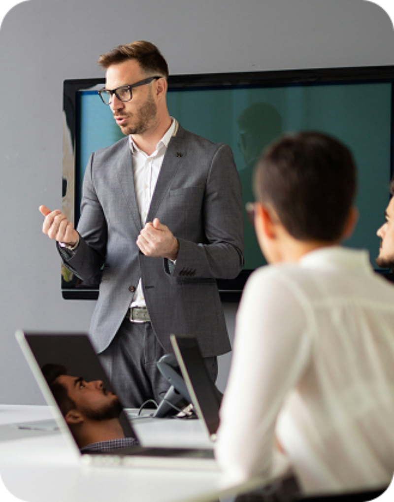 Homme debout en costume qui prend la parole lors d'une réunion d'équipe
